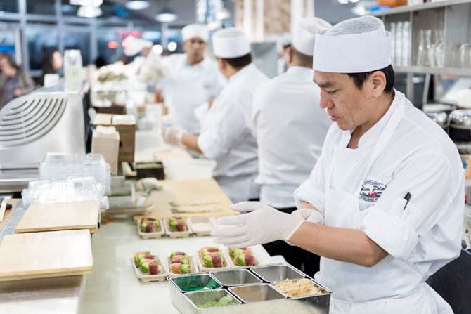line of chefs preparing and handling food in a large kitchen