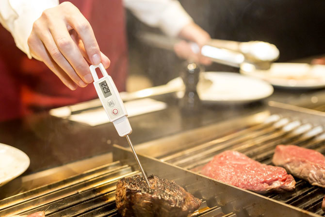 kitchen employee checking food temperatures for meat
