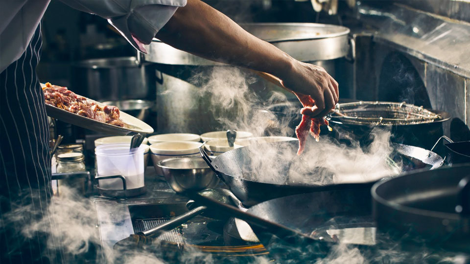 chef safely cooking meat in a large restaraunt kitchen