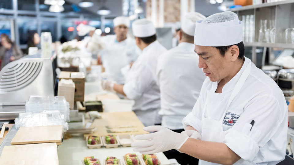 line chefs in kitchen preparing food while wearing safety gloves