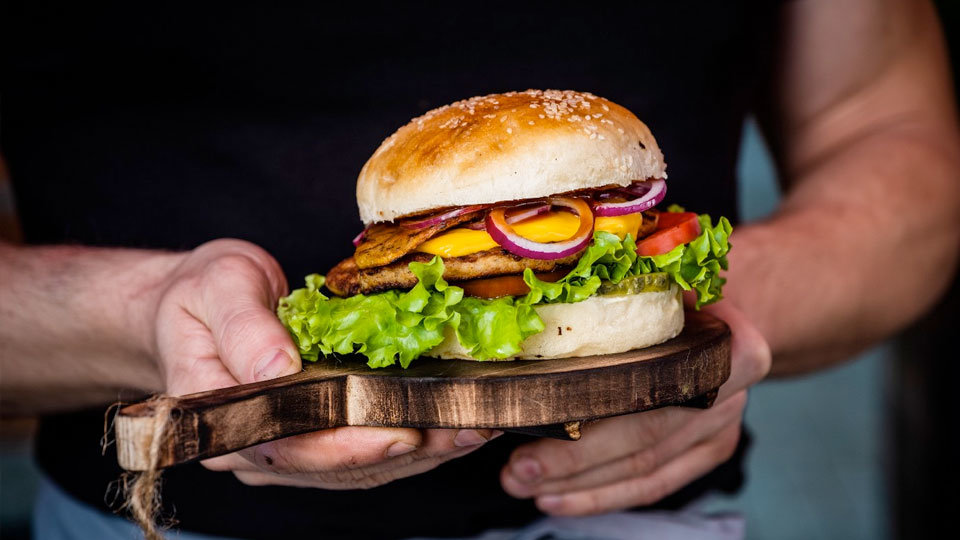 server at restaurant carrying loaded burger on wooden plate